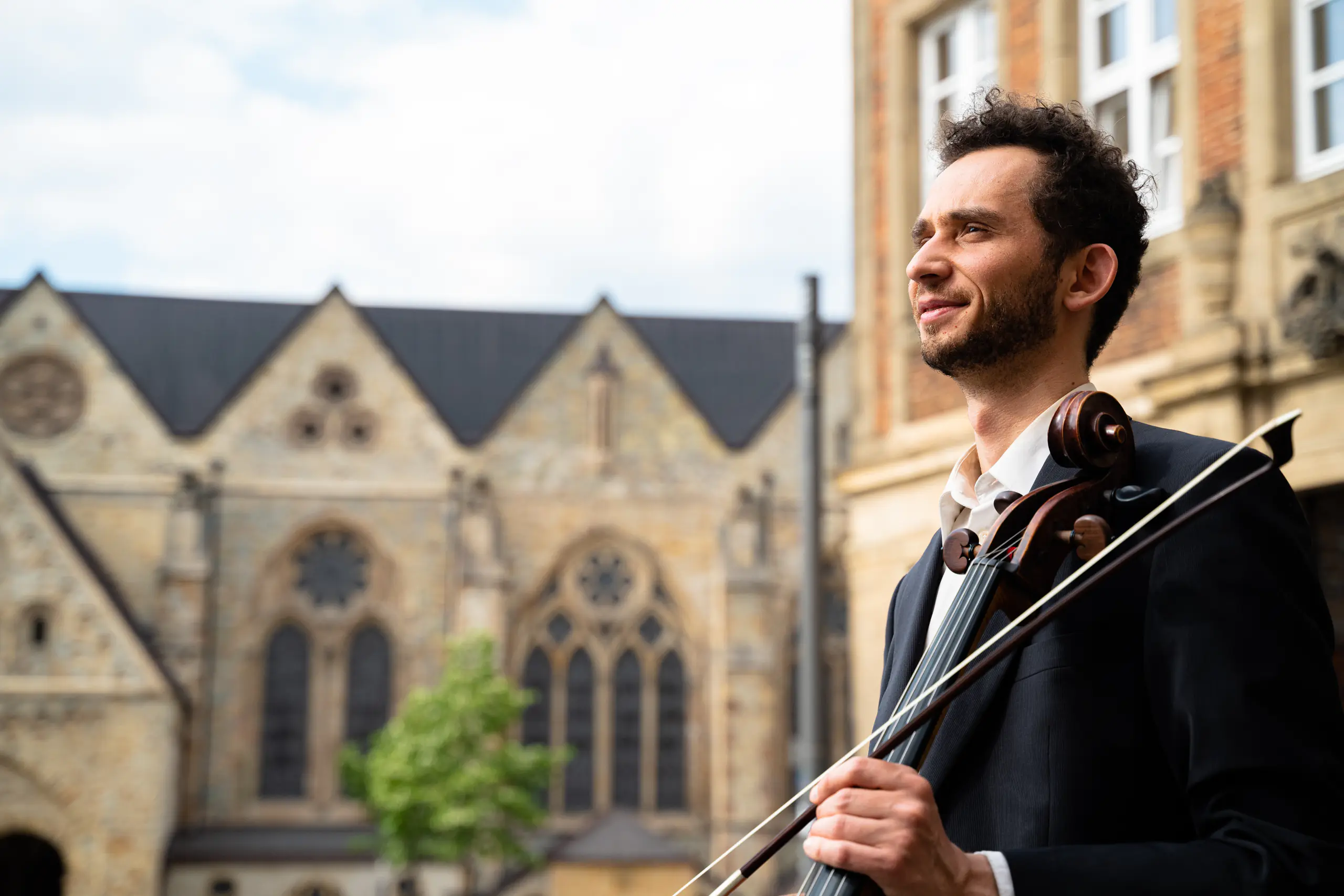 Ventsislav Harkov holding his cello and bow in front of a Gothic church
