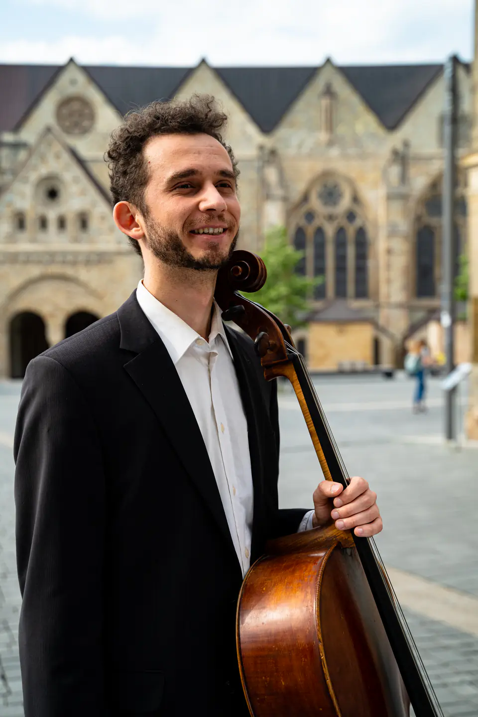 Ventsislav Harkov smiling with his cello, a cathedral in the background