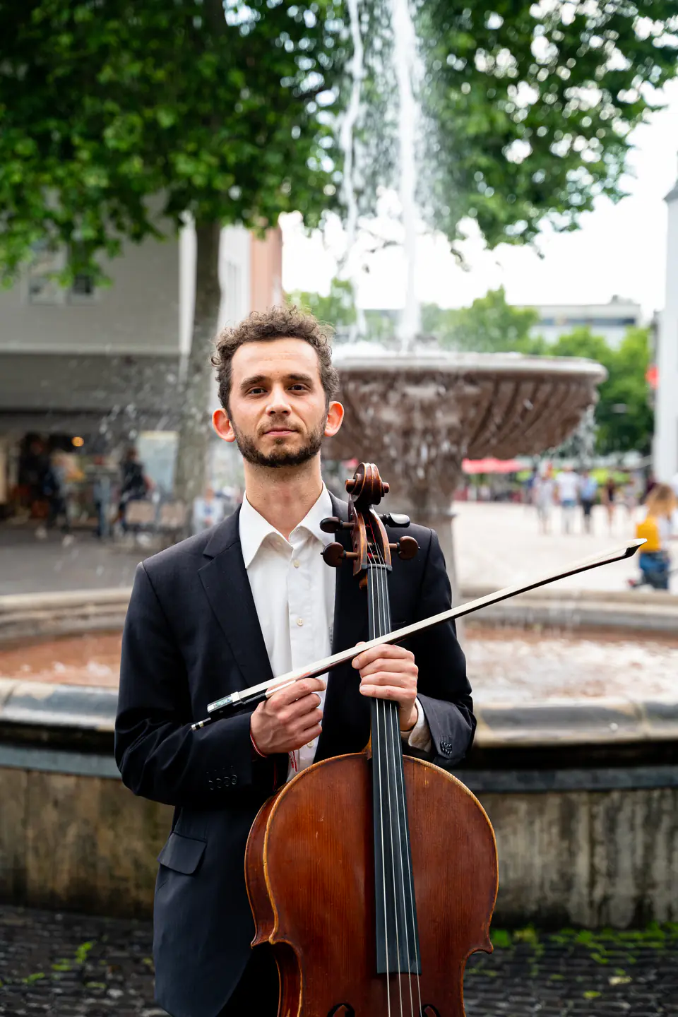 Ventsislav Harkov with his cello and bow in front of a fountain