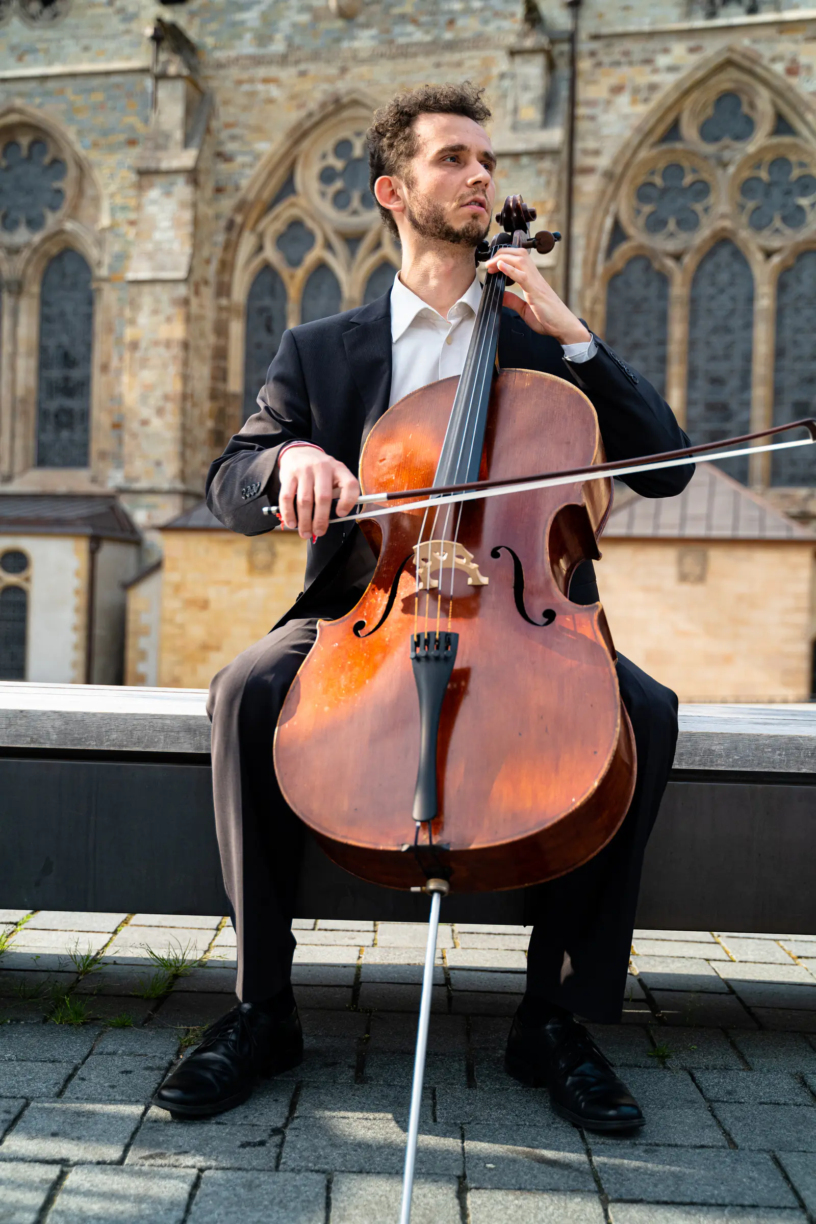 Ventsislav Harkov playing the cello in front of the Gothic windows of a church