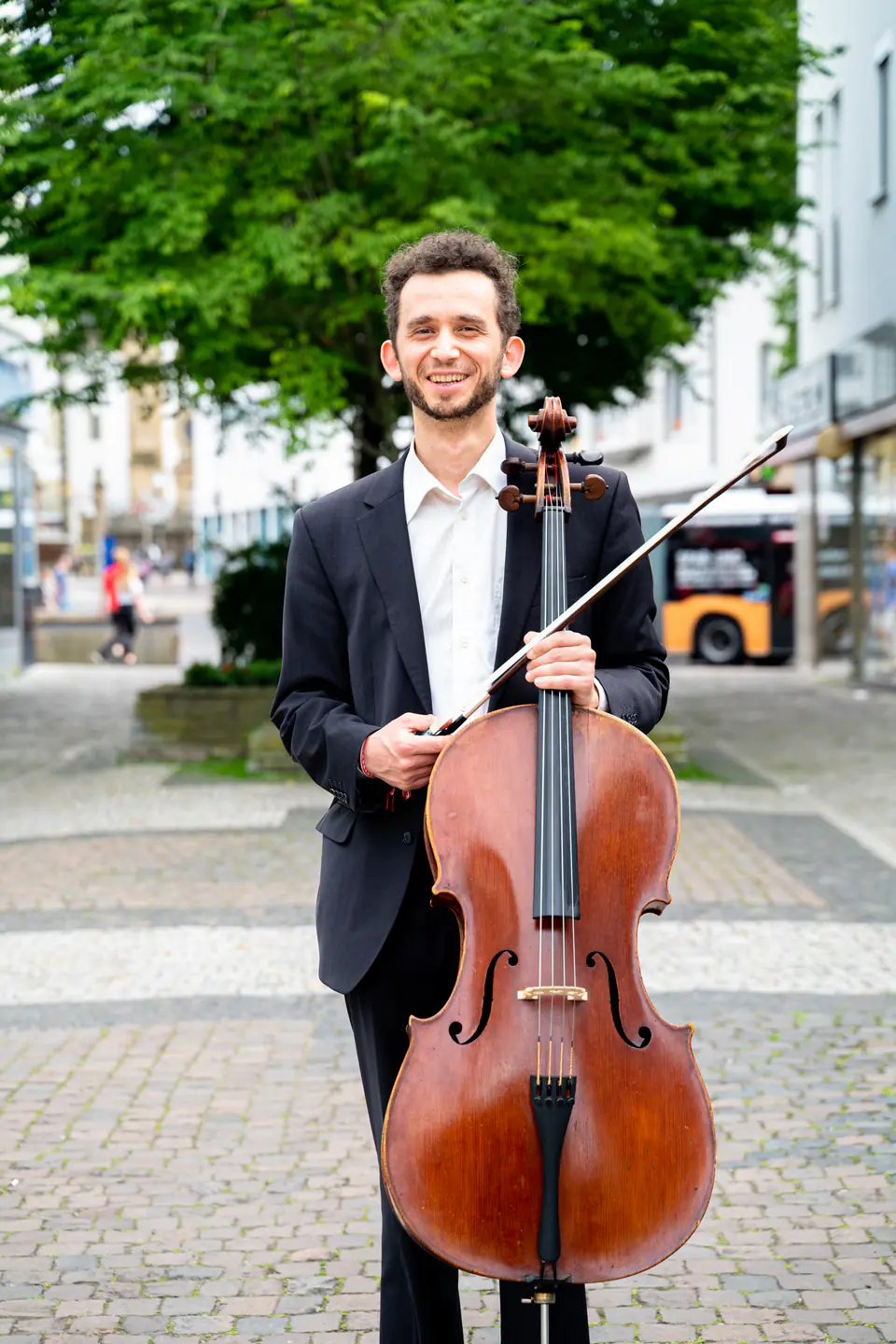 Ventsislav Harkov smiling with his cello and bow in a pedestrian street