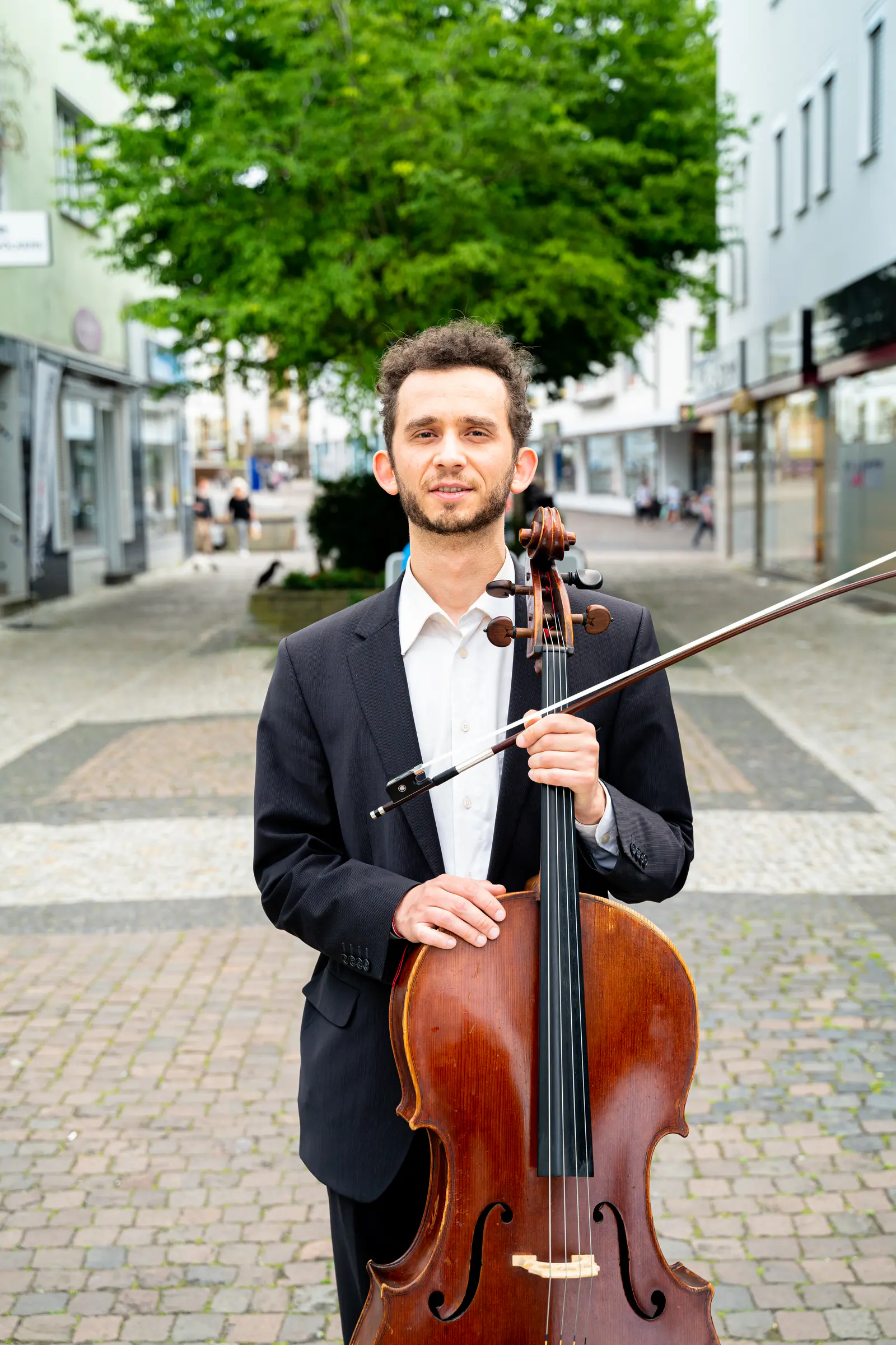Ventsislav Harkov with his cello and bow under a tree in a pedestrian street