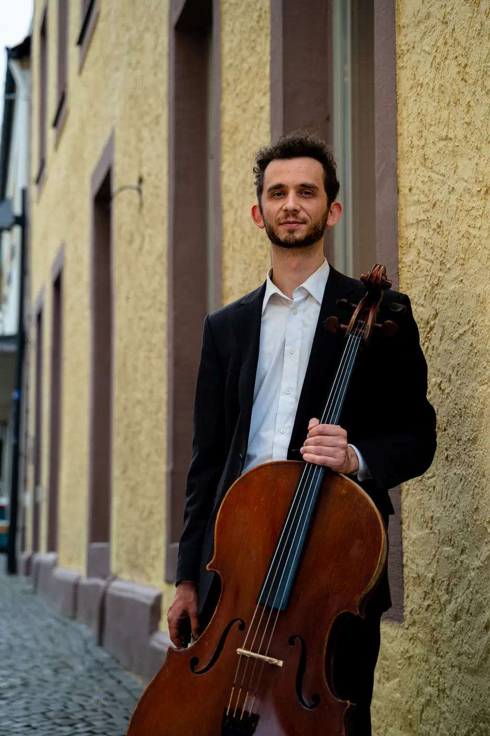 Ventsislav Harkov with his cello in front of a yellow wall